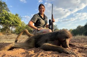 Lady posing with a baboon that she has shot.
